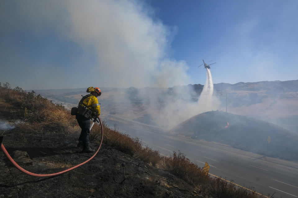 A firefighter works on hotspots as a helicopter drops water at a wildfire in Castaic, Calif., on Wednesday, Aug. 31, 2022. (AP Photo/Ringo H.W. Chiu)