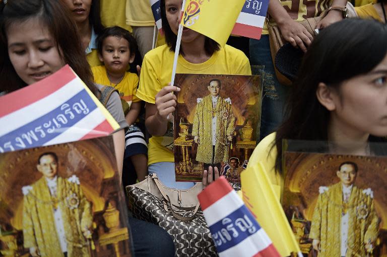 Thai well-wishers hold portraits of King Bhumibol Adulyadej and wave flags as they gather at Siriraj Hospital where the king has spent most of the last few months, on the occasion of his 87th birthday in Bangkok on December 5, 2014