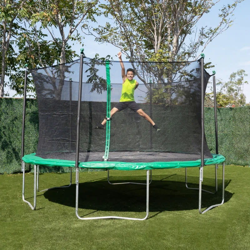 Child mid-jump on outdoor trampoline with safety net, smiling, hands and legs spread out