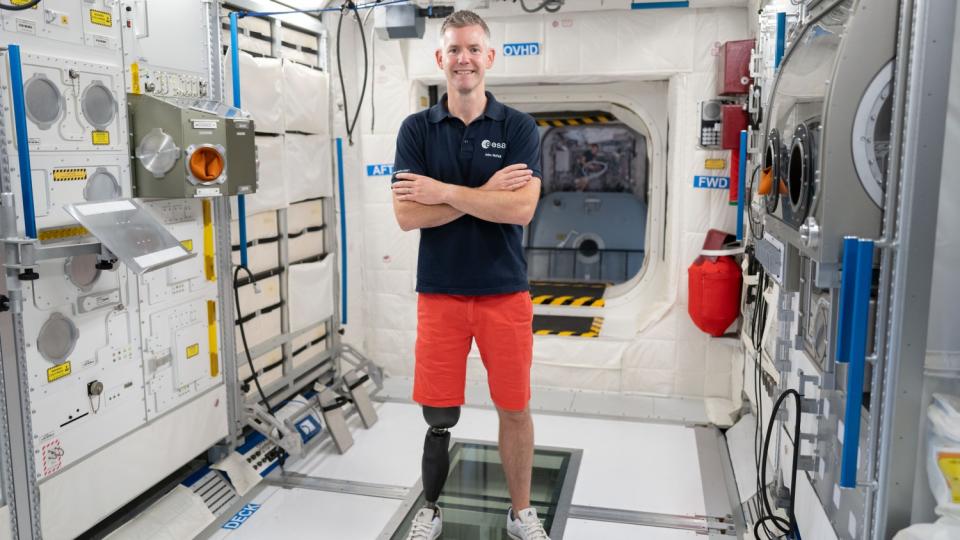 ein Astronaut, der mit einer Prothese am rechten Bein in einem ISS-Modul steht