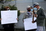 A protestor holds a cross and passes in front of other protestors with banners reading in Greek "The satanist does not represent us", outside Cyprus' national broadcasting building, during a protest, in capital Nicosia, Cyprus, Saturday, March 6, 2021. The Orthodox Church of Cyprus is calling for the withdrawal of the country’s controversial entry into this year’s Eurovision song context titled “El Diablo”, charging that the song makes an international mockery of country’s moral foundations by advocating “our surrender to the devil and promoting his worship.” (AP Photo/Petros Karadjias)