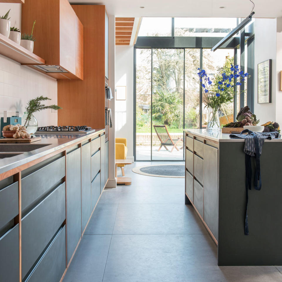 black and wooden kitchen with glass sliding doors next to a black island with a white counter topped with vegetables and flowers