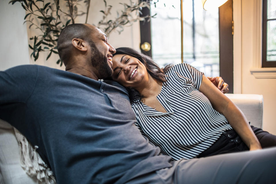 A couple laughs together as they cuddle on a couch