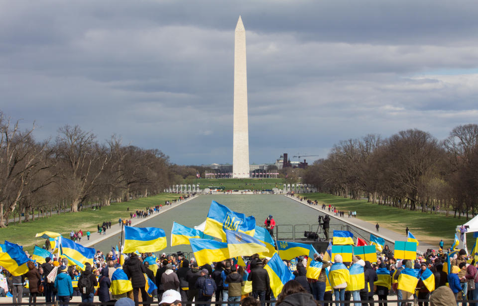 A sea of yellow and blue Ukrainian flags group in support of Ukraine, with the stone obelisk in the background.