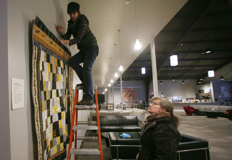Alice McGary and Greta Anderson install photos and quilts for an upcoming art show at Harvest Vineyard Church of Ames. A free public reception to kick off the community art show will be held Saturday from 6 p.m. to 8 p.m.
