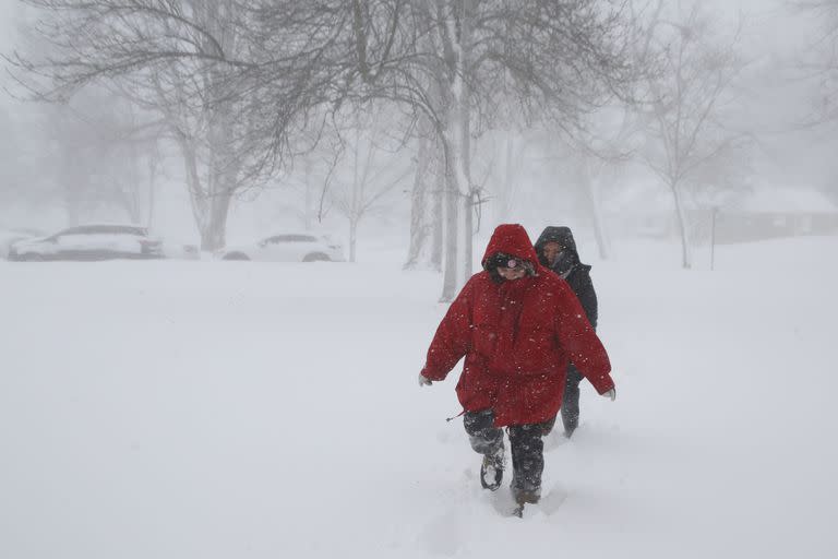 Dos personas caminan por la calle mientras una tormenta de invierno atraviesa el oeste de Nueva York el sábado, 24 de diciembre de 2022, en Amherst, Nueva York.