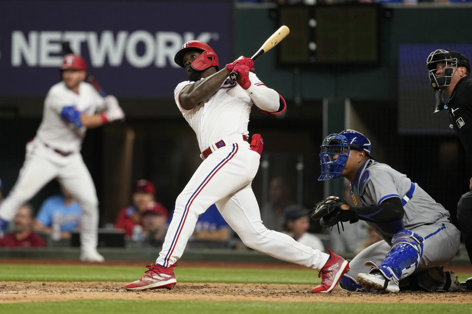 Texas Rangers' Adolis Garcia, front left, follows through on a grand slam swing as Kansas City Royals catcher Salvador Perez, front center, and umpire Cory Blaser, right, look on in the sixth inning of a baseball game, April 10, 2023, in Arlington, Texas. (AP Photo/Tony Gutierrez)