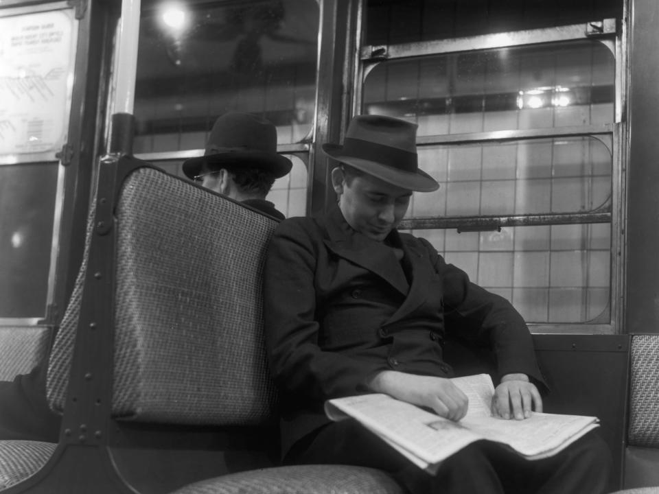 A man holding a newspaper in his lap sleeps while riding a subway on the Eighth Avenue line in New York City.