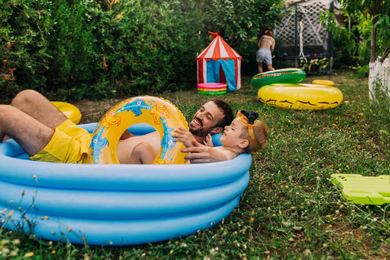 father and son relaxing in kiddie pool in backyard