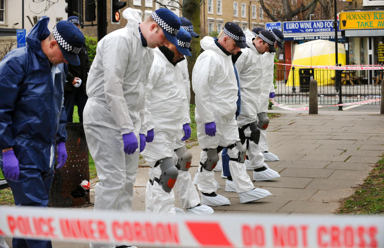 Crime scene officers search for evidence in the park opposite the Euro Wine & Food Store (rear) in Hornsey Road, north London, where a father and son were the victims of a drive-by shooting. 