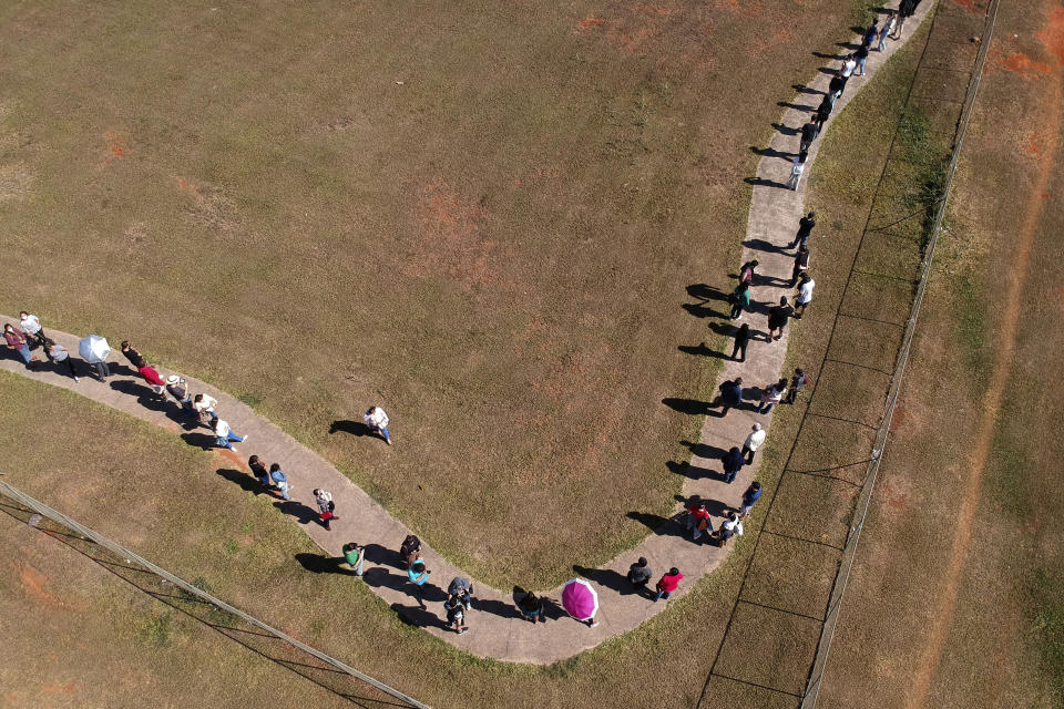 A line of people snakes around a field to enter a COVID-19 vaccination site, as people over age 30 became eligible for a vaccine in Brasilia, Brazil, Tuesday, Aug. 3, 2021. (AP Photo/Eraldo Peres)