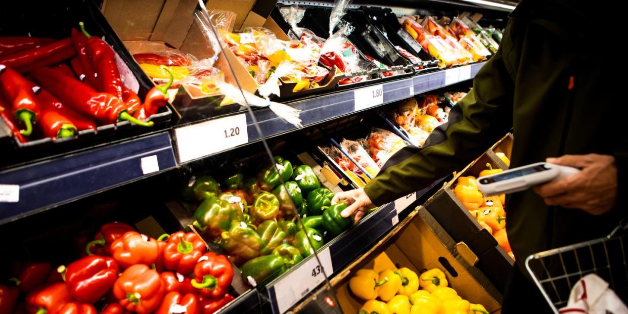 person reaching for green peppers in vegetable aisle