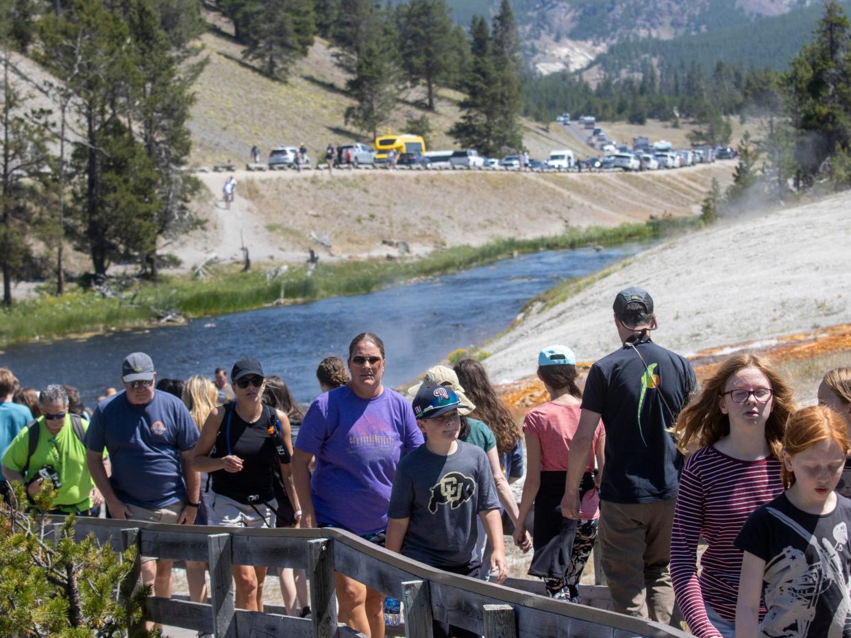 A long line of people on a trail at Yellowstone, with a river in the background and a road full of cars.