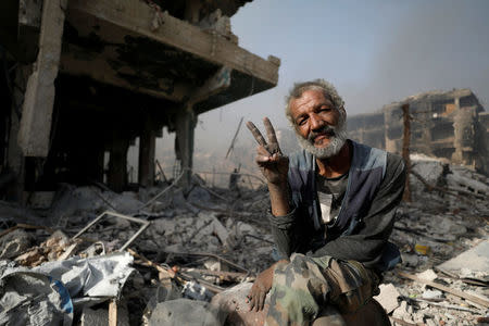 A man gestures as he sits on the rubble of damaged buildings in al-Hajar al-Aswad, Syria May 21, 2018. REUTERS/Omar Sanadiki