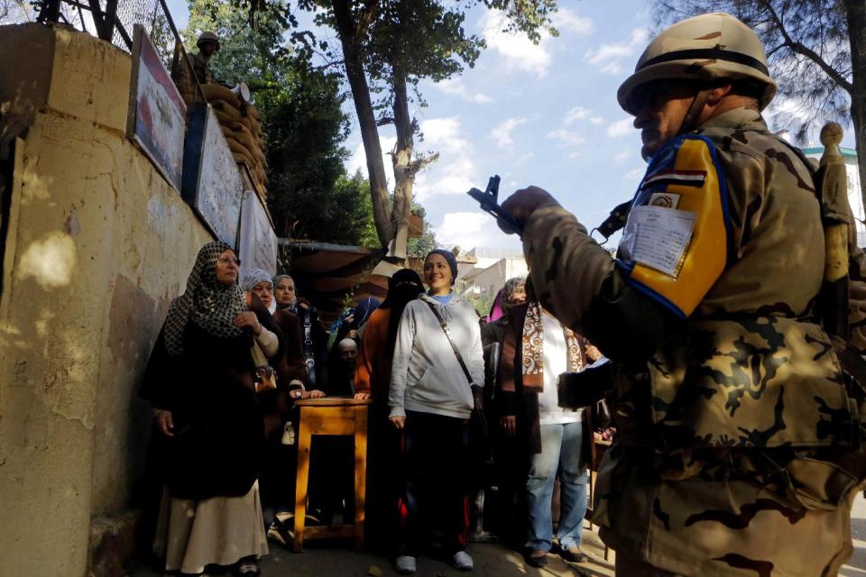 An Egyptian soldier stands guard in front of voters outside a polling station in the Maadi neighborhood of Cairo, Egypt, Tuesday, Jan. 14, 2014. Egyptians are voting on a draft for their country's new constitution that represents a key milestone in a military-backed roadmap put in place after President Mohammed Morsi was overthrown in a popularly backed coup last July. (AP Photo/Amr Nabil)