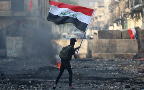 An Iraqi anti-government protester waves a national flag close to a concrete barricade amidst clashes with security forces along the capital Baghdad's Rasheed street - Credit: AFP