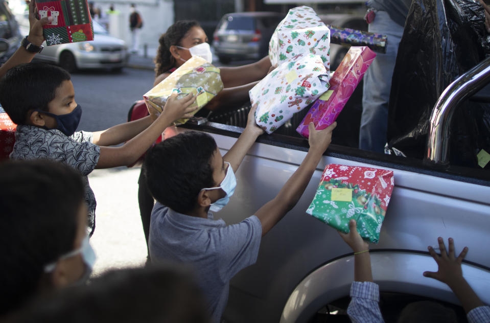 Children receive Christmas presents donated by the volunteer group "Un Juguete, Una Buena Noticia," or One Toy, One Good News, from the back of a pick-up truck in Caracas, Venezuela, Friday, Dec. 18, 2020. The volunteer group is made up of journalists and other media workers who collect donations and hand out toys to poor children. (AP Photo/Ariana Cubillos)