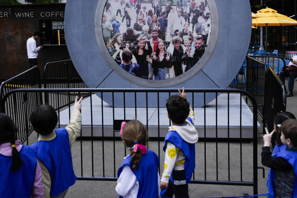 Children signal to pedestrians in Dublin, Ireland, through a livestream portal as part of an art installation on the street in New York, Tuesday, May 14, 2024. (AP Photo/Seth Wenig)