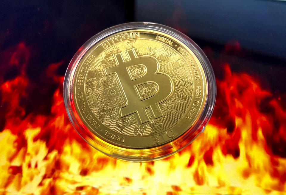 A stylised image of a physical bitcoin floating above flames. Source: AP