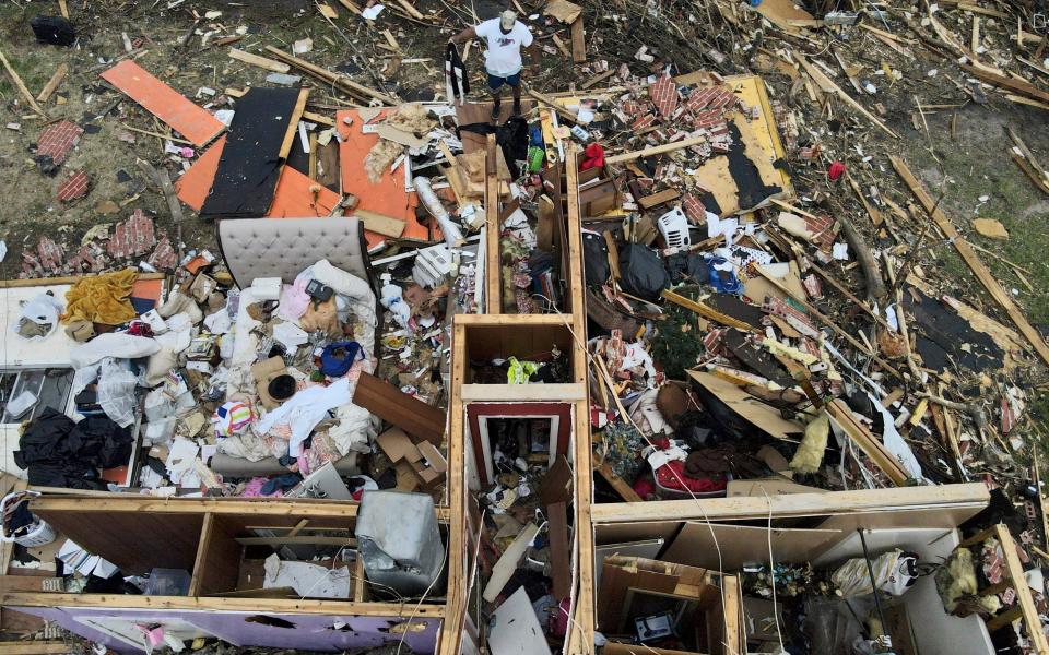 A man, top center, salvages a jacket as he looks over a tornado damaged home in Rolling Fork - AP Photo/Julio Cortez