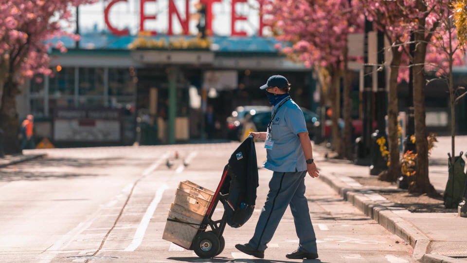 Seattle, USA – April 13, 2020: Late in the day a mailman wearing a mask crossing the street by Pike Place Market at the height of the Coronavirus city wide shutdown.