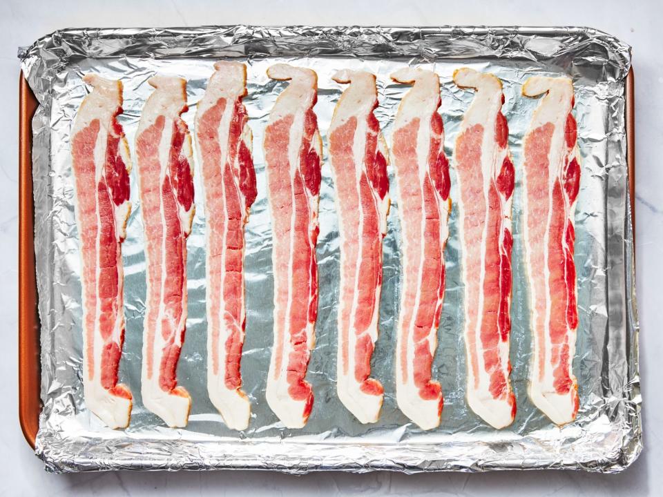 uncooked bacon on an aluminum foil-lined pan