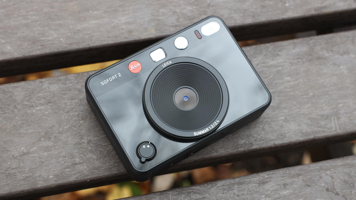  Leica Sofort 2 hybrid camera laying down on a slatted wooden table. 