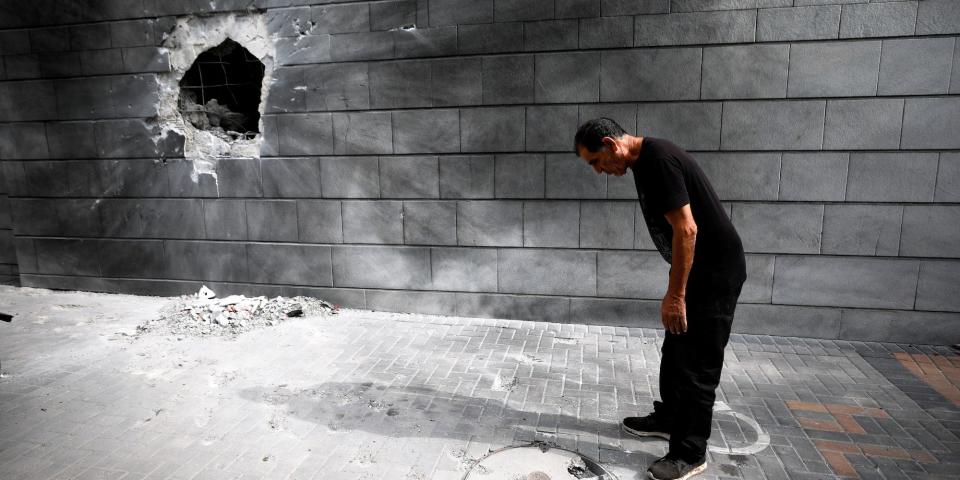 A man in Ashkelon, Israel, looks at the ground near a wall that has a hole blasted in it by a rocket