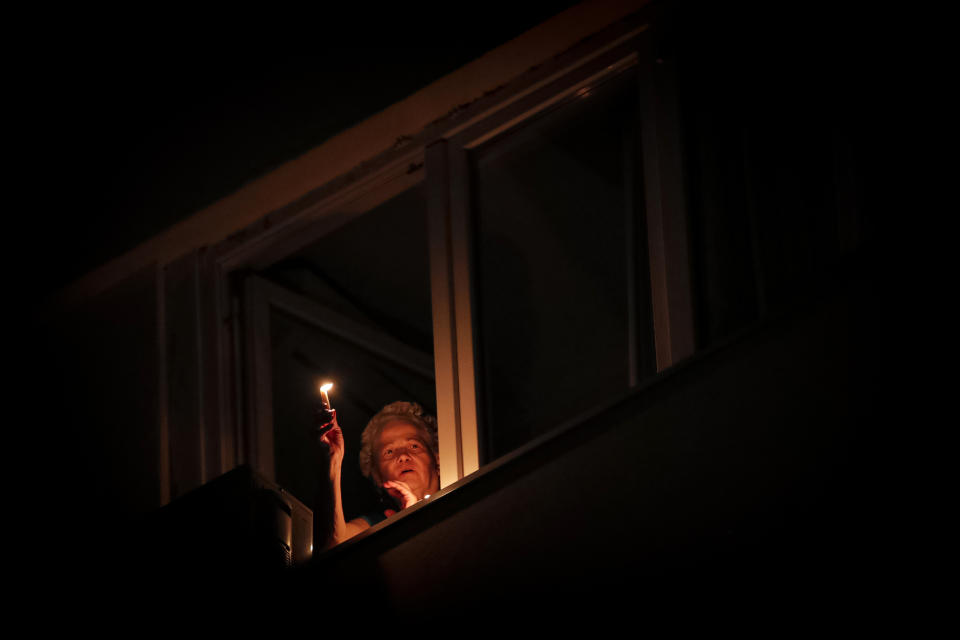 A woman holds a candle at the window while listening to the blessings of a priest from downstairs during the coronavirus pandemic in Bucharest, Romania, Saturday, April 18, 2020. Priests accompanied by volunteers distributed the holy light ahead of the usual time, at midnight, as people observed the interdiction to join religious celebrations in the week leading to the Orthodox Easter, imposed across Romania as authorities try to limit the spread of the COVID-19 infections. (AP Photo/Vadim Ghirda)