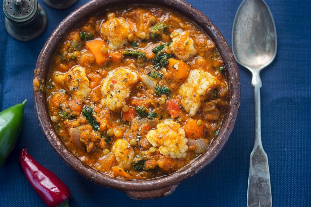 Vegetable dhal in brown stone bowl with silver spoon and whole red and green chili peppers on navy blue tablecloth