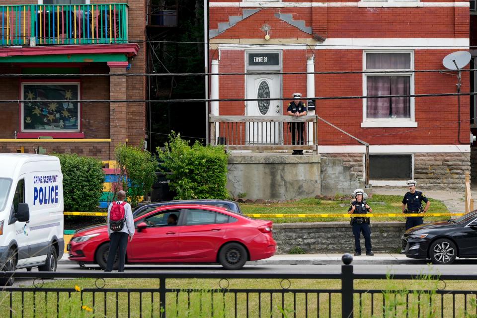 Police officers stand behind caution tape marking off several houses outside of the scene of a suspected homicide at 1748 Queen City Ave. in the South Fairmount neighborhood of Cincinnati on Monday,