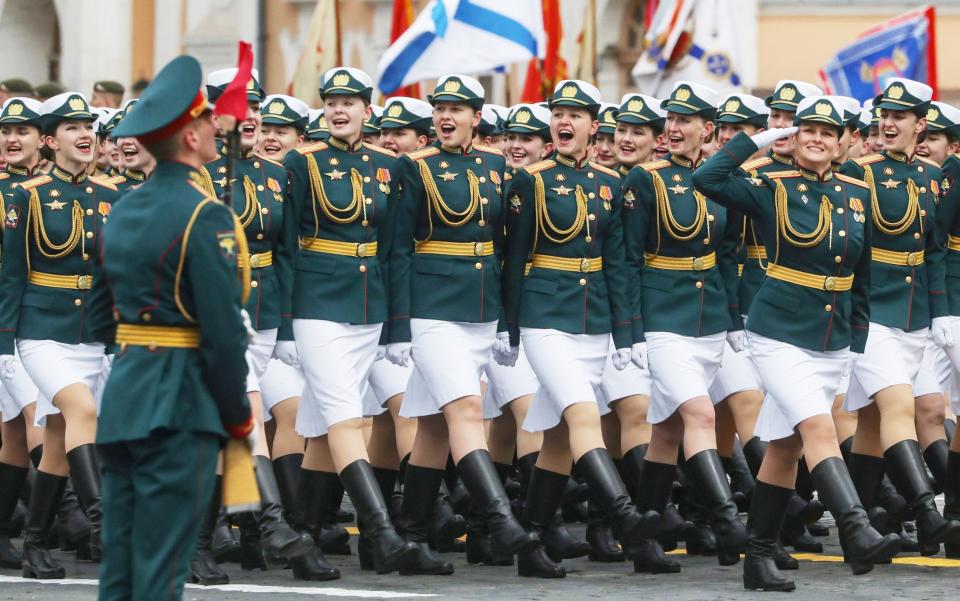 Female soldiers smile as they turn to face Putin while marching past in military uniforms and short, white skirts