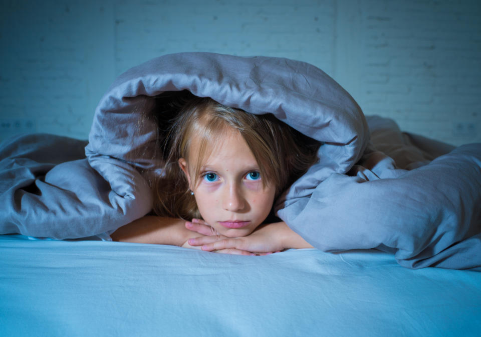 Cute little caucasian girl lying in bed covering her head with blanket feeling exhausted and sleepless suffering from insomnia Depression Stress in Children Emotional and Sleeping Disorders concept.