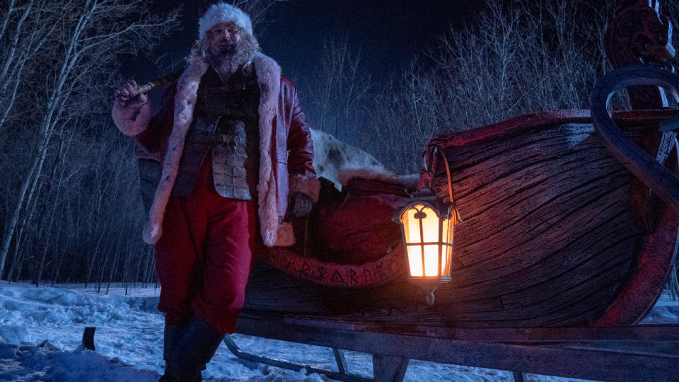 David Harbour stands next to his sleigh, with his sledgehammer on his shoulder, in Violent Night.