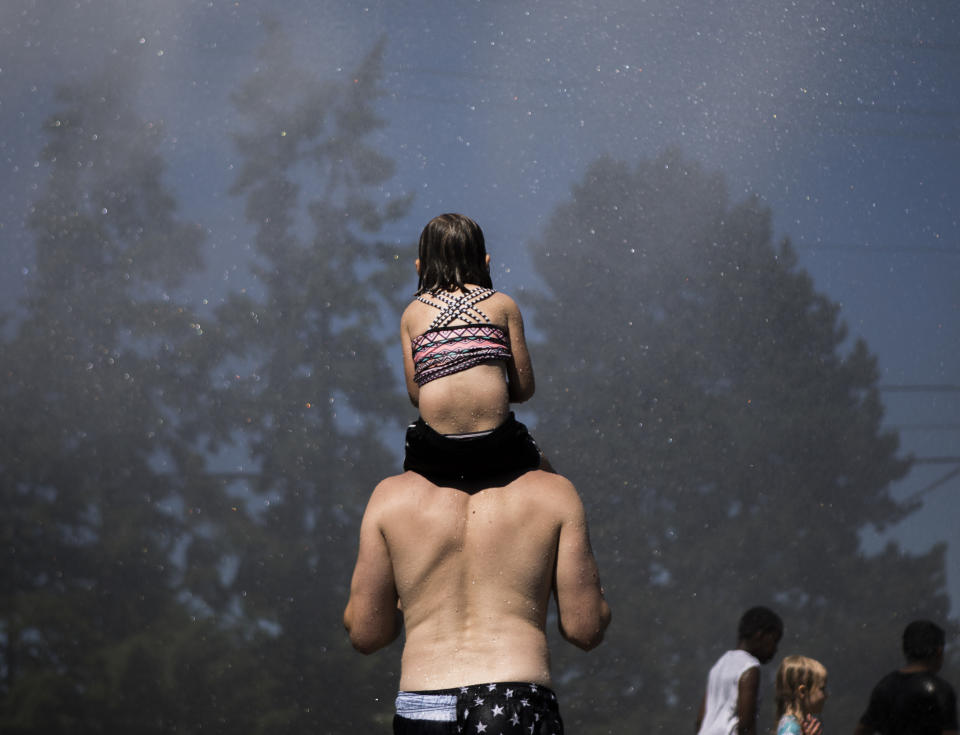 People stand in the spray from the Everett Fire Department's fire hose sprinkler station at Walter E. Hall Park on Saturday, June 26, 2021 in Everett, Wa. (Olivia Vanni/The Daily Herald via AP)