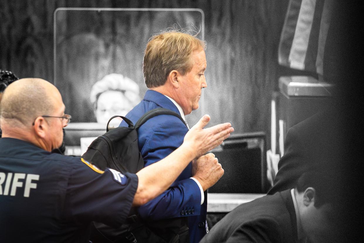 Ken Paxton, in a suit and wearing a black backpack, is escorted by a sheriff through the Capitol building.