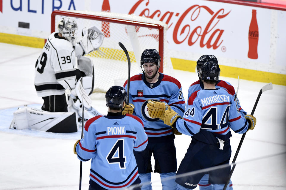 Winnipeg Jets center Sean Monahan celebrates his goal on Los Angeles Kings goaltender Cam Talbot (39) with Neal Poink (4) and Josh Morrissey (44) during the second period of an NHL hockey game in Winnipeg, Manitoba, on Monday, April 1, 2024. (Fred Greenslade/The Canadian Press via AP)