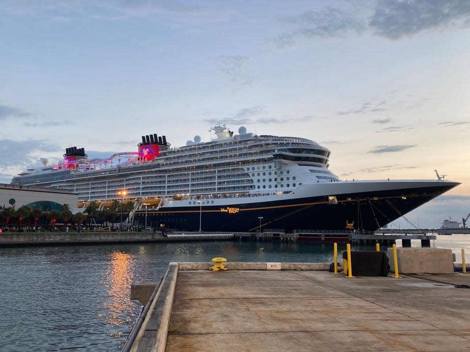 Huge Disney Wish cruise ship docked at dusk.