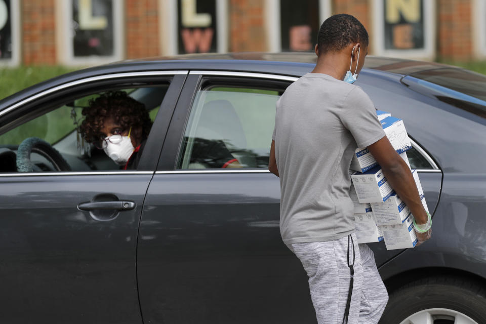 Tre Shields, 15, loads boxes of protective face masks in the backseat for Loretta Striplin, left, of St. Paul AME church as Striplin picks up protective equipment for her congregation Thursday, May 28, 2020, in Hanley Hills, Mo. The masks were provided by St. Louis city and county and by the state of Missouri as area churches prepare to restart services as restrictions surrounding the coronavirus outbreak ease. (AP Photo/Jeff Roberson)