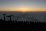 People gather around a torii gate as they watch the sunrise from the summit of Mount Fuji, Saturday, Aug. 3, 2019, in Japan. (AP Photo/Jae C. Hong)