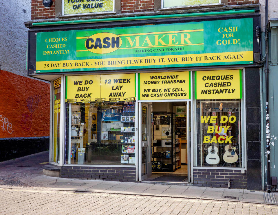 An image of a pawn shop with a green and yellow shop front with many signs, with things like "We do buy back" and "cash for gold!" written on them