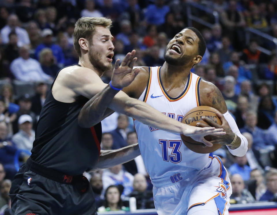 Oklahoma City Thunder forward Paul George (13) is fouled by Portland Trail Blazers forward Jake Layman, left, as he drives to the basket in the first half of an NBA basketball game in Oklahoma City, Monday, Feb. 11, 2019. (AP Photo/Sue Ogrocki)