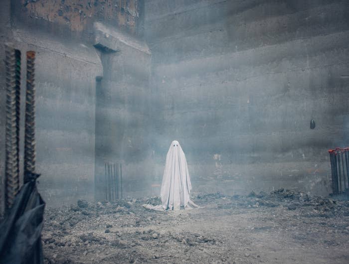 a classic ghost under a bedsheet standing in the middle of a worksite from the movie a ghost story