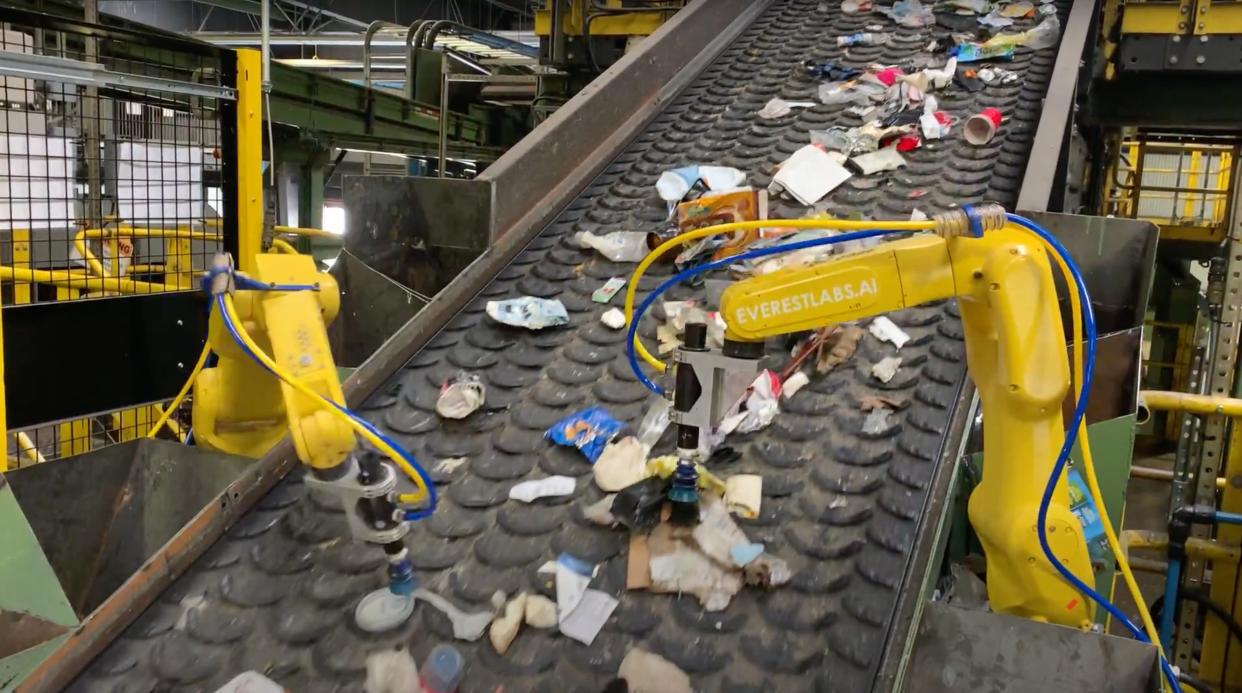 Yellow robotic arms sort recyclables on a conveyer belt.