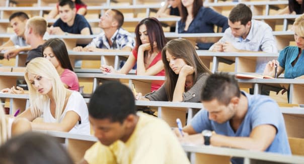 'Group of college students in the university amphitheatre, they are sitting and doing an exam.'