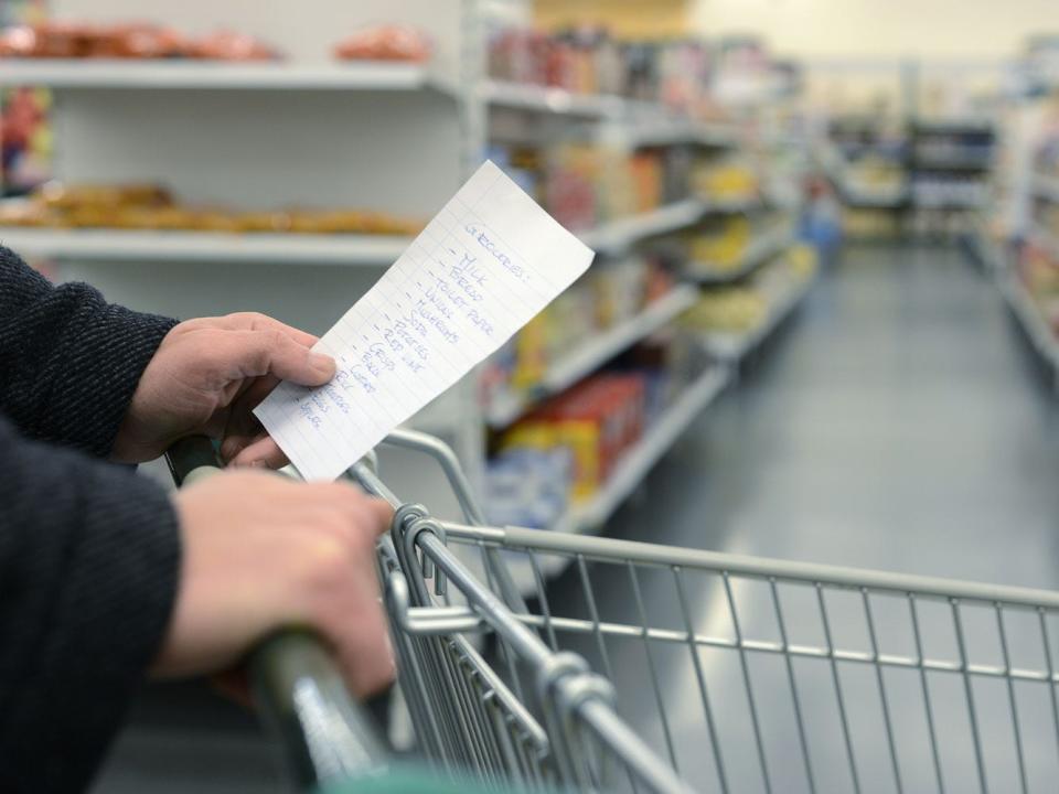 hands holding a shopping list while pushing a grocery cart