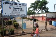 Girls walk past a billboard with Chevron's corporate logo at the Berthy Rios school in La Canada de Urdaneta