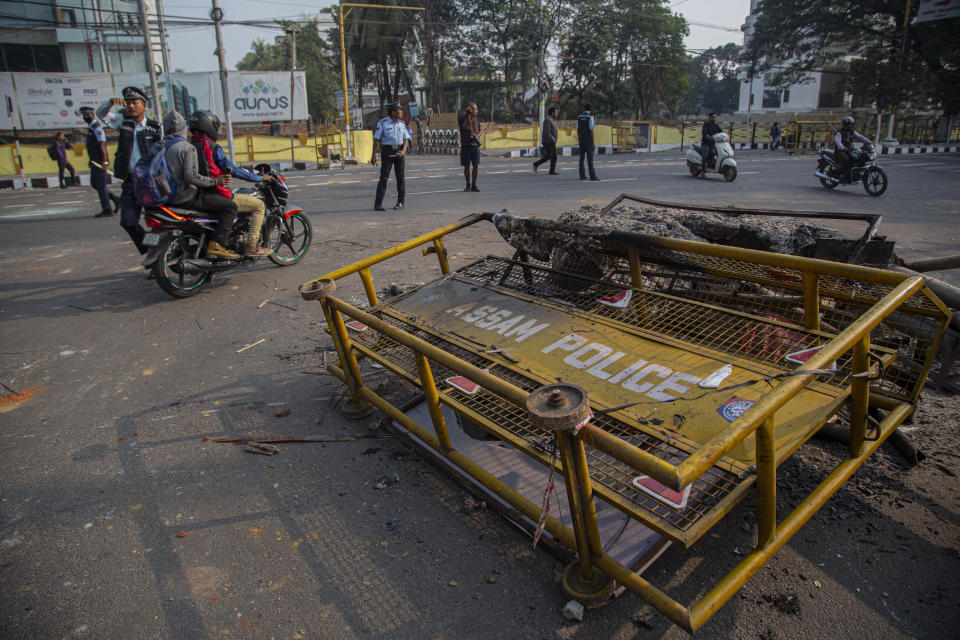 People ride past police barricades damaged by protestors in Gauhati, India, Thursday, Dec. 12, 2019. Police arrested dozens of people and enforced curfew on Thursday in several districts in India’s northeastern Assam state where thousands protested legislation granting citizenship to non-Muslims who migrated from neighboring countries. (AP Photo/Anupam Nath)