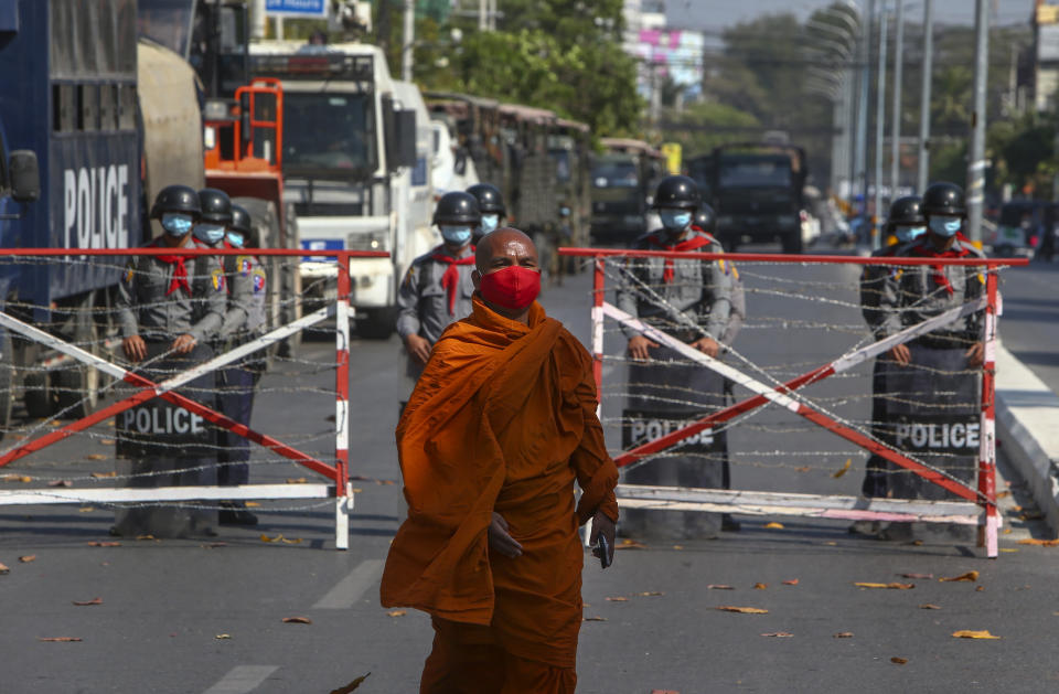 A Buddhist monk walks along a road as police stand watch in Mandalay, Myanmar, Wednesday, Feb. 24, 2021. Protesters against the military's seizure of power in Myanmar were back on the streets of cities and towns on Wednesday, days after a general strike shuttered shops and brought huge numbers out to demonstrate. (AP Photo)