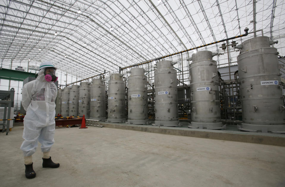 FILE - In this Nov. 12, 2014, file photo, a Tokyo Electric Power Co. (TEPCO) official wearing a radioactive protective gear stands in front of Advanced Liquid Processing Systems during a press tour at the Fukushima Dai-ichi nuclear power plant in Okuma, Fukushima Prefecture, northeastern Japan. Japan revised a roadmap on Friday, Dec. 27, 2019, for the tsunami-wrecked Fukushima nuclear plant cleanup, further delaying the removal of thousands of spent fuel units that remain in cooling pools since the 2011 disaster. (AP Photo/Shizuo Kambayashi, Pool, File)